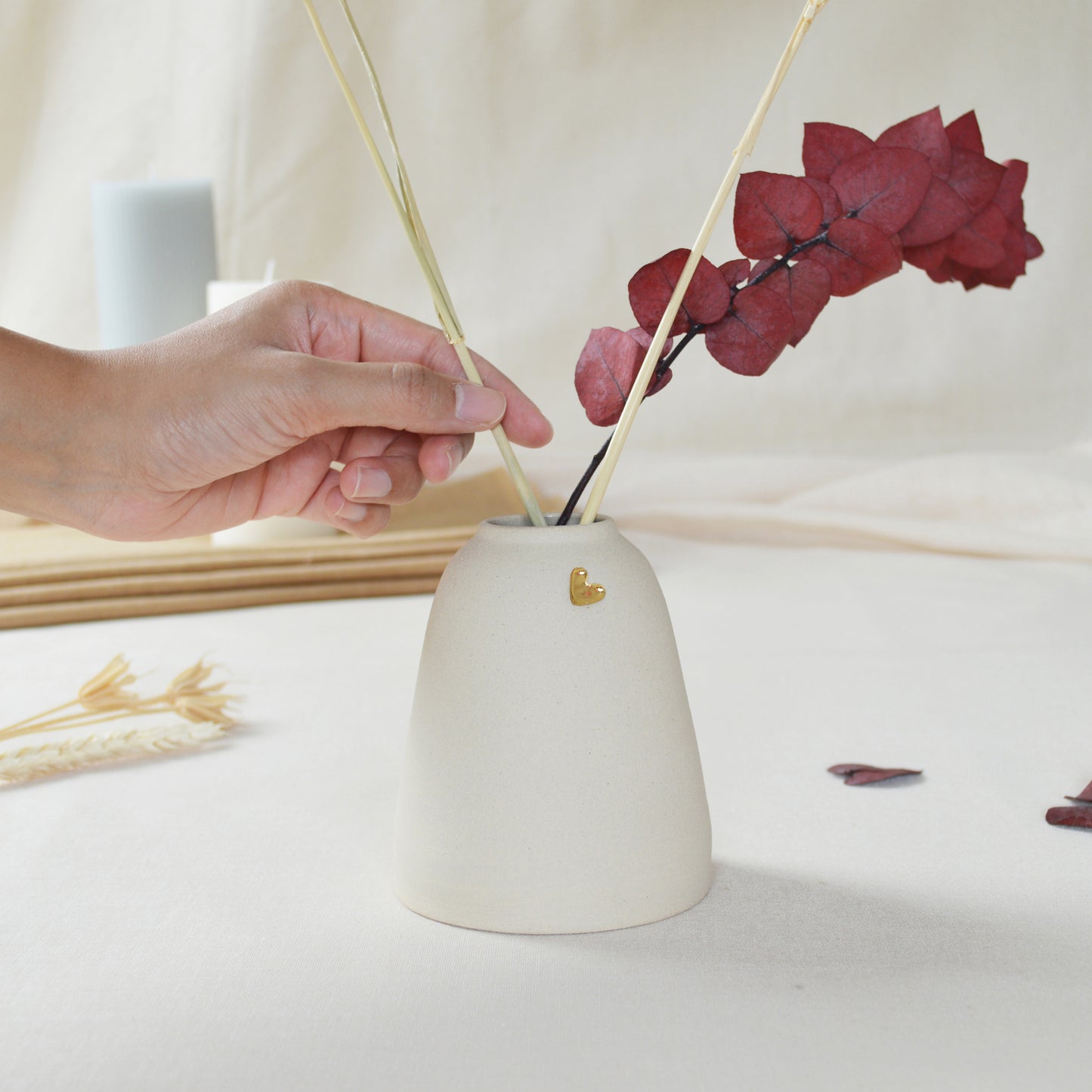 Handmade cream ceramic vase with a short rim and gold heart. Hand placing dried flowers in the vase.