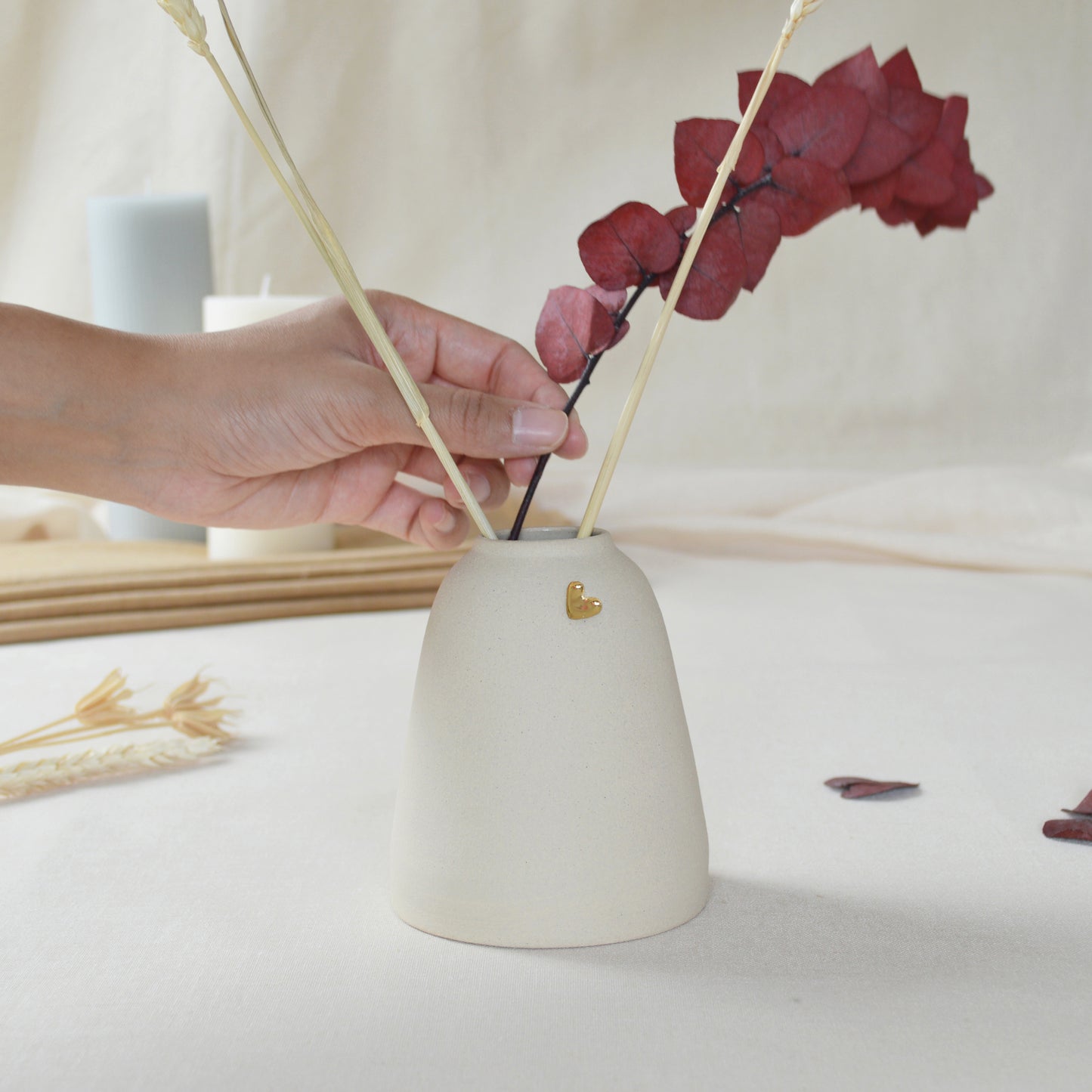 Handmade cream ceramic vase with a short rim and gold heart. Hand placing dried flowers in the vase.