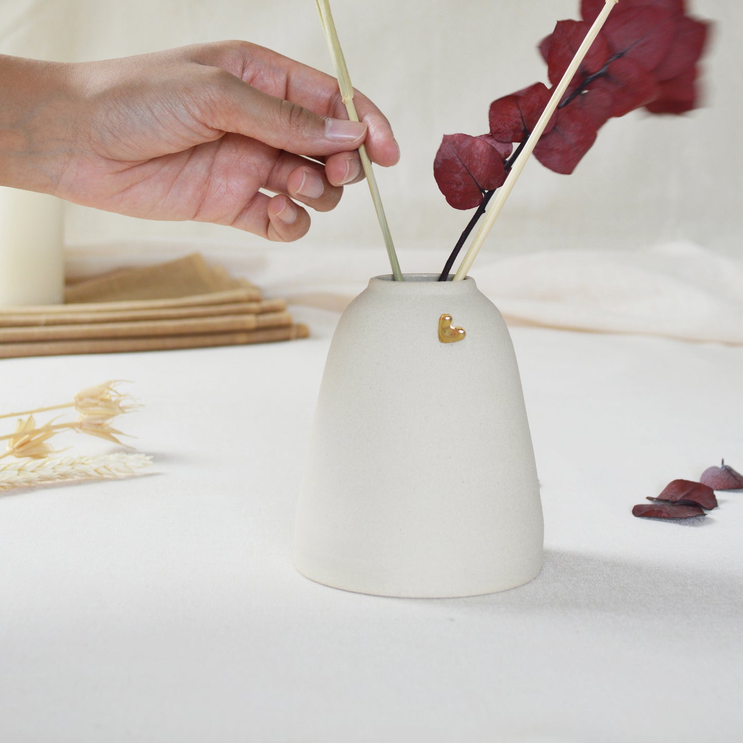 Handmade cream ceramic vase with a short rim and gold heart. Hand placing dried flowers in the vase.