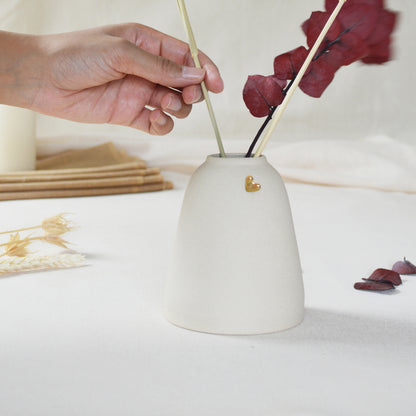 Handmade cream ceramic vase with a short rim and gold heart. Hand placing dried flowers in the vase.